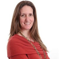A woman with long brown hair wearing a red blouse smiles for a portrait in front of a white background.