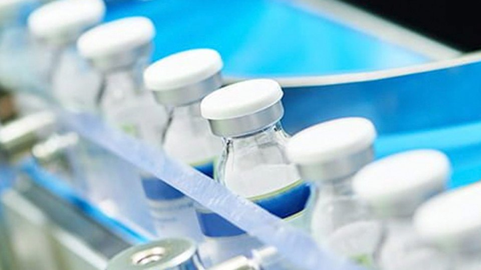 A row of sealed glass vials moving along an automated pharmaceutical production line.